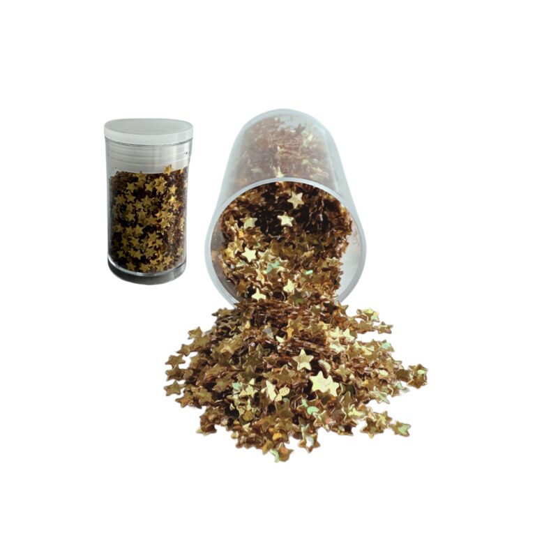 Złote gwiazdy dekoracyjne w plastikowym pojemniku, część wysypana na biały blat, błyszczące i połyskujące w świetle.